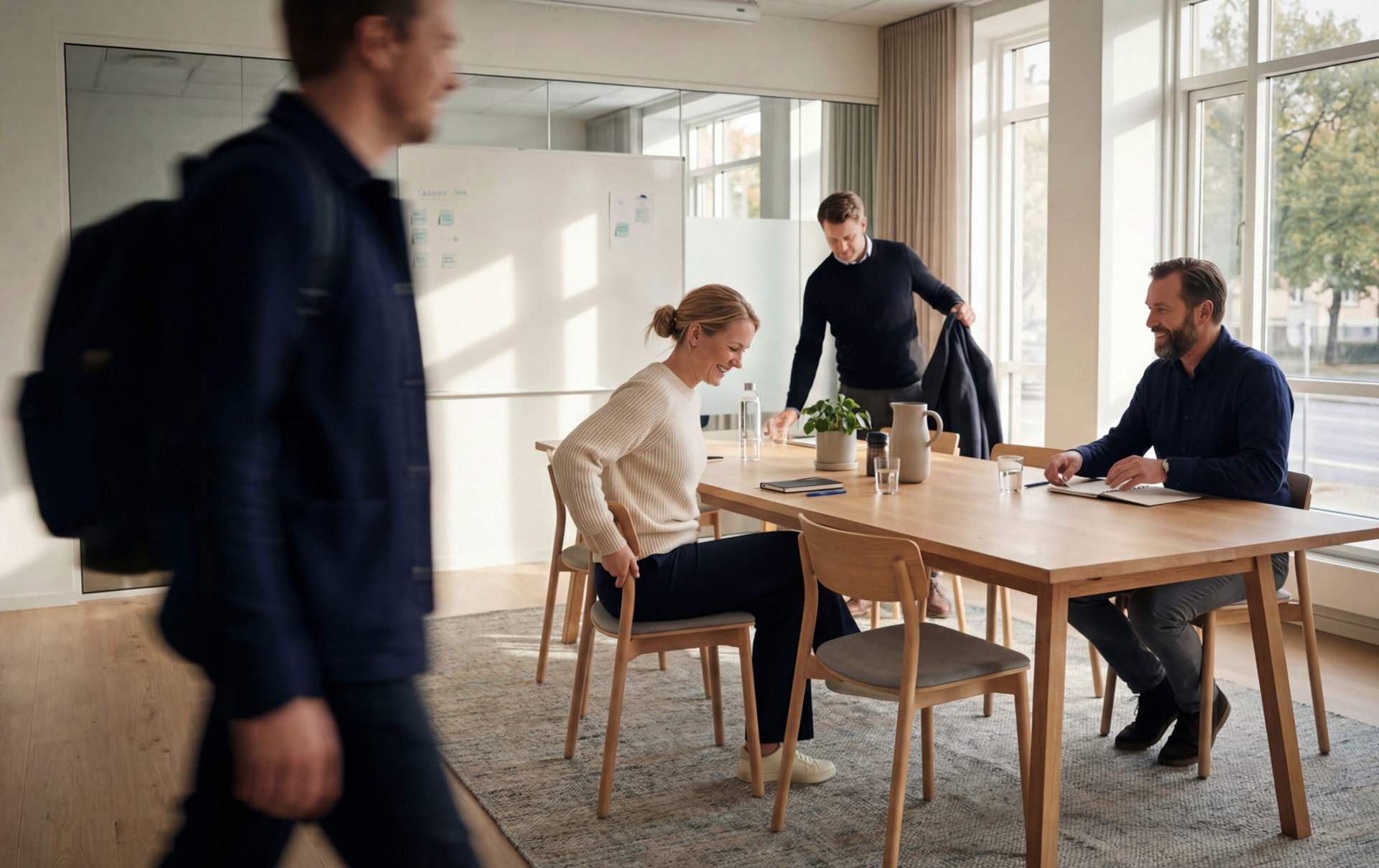 Meetingraum, eine Person läuft durch das Bild, drei Personen setzen sich an den Tisch
